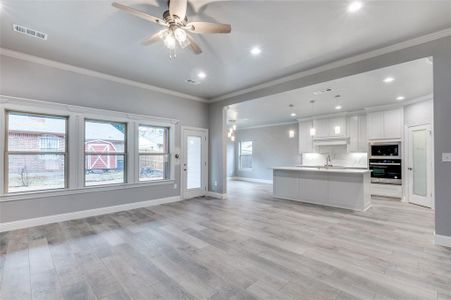 Kitchen featuring white cabinetry, an island with sink, sink, hanging light fixtures, and light hardwood / wood-style flooring