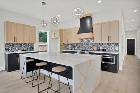 Kitchen featuring premium range hood, light brown cabinetry, a center island with sink, and appliances with stainless steel finishes