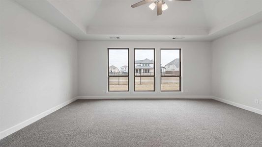 Carpeted spare room featuring a tray ceiling and ceiling fan