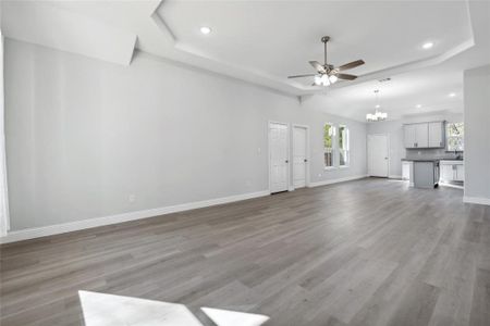 Unfurnished living room with a raised ceiling, ceiling fan with notable chandelier, and light hardwood / wood-style flooring