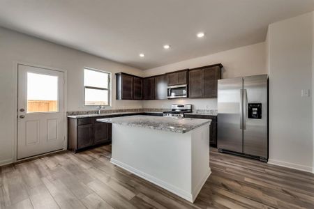 Kitchen with light hardwood / wood-style flooring, stainless steel appliances, dark brown cabinetry, a kitchen island, and light stone countertops