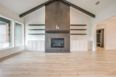 Unfurnished living room featuring light hardwood / wood-style flooring, beamed ceiling, and high vaulted ceiling