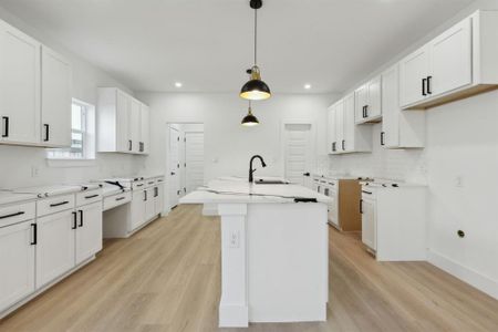 Kitchen with white cabinetry, decorative light fixtures, and a kitchen island with sink