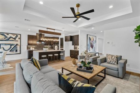 Living room with ceiling fan, a tray ceiling, and light wood-type flooring