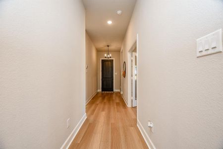 This photo shows a bright hallway with light wood flooring, neutral walls, and a ceiling light fixture. It leads to a dark door at the end, with a side room visible on the right. This photo shows a bright hallway with light wood flooring, neutral walls, and a ceiling light fixture. It leads to a dark door at the end, with a side room visible on the right.