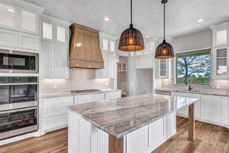 Kitchen with custom range hood, stainless steel appliances, a kitchen island, sink, and white cabinetry