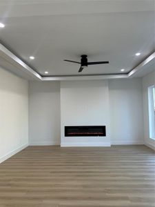 Unfurnished living room featuring ceiling fan, a raised ceiling, and light wood-type flooring