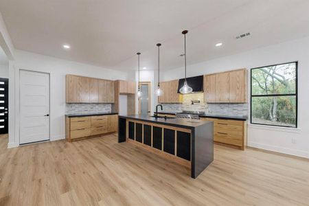 Kitchen featuring extractor fan, pendant lighting, light hardwood / wood-style flooring, a center island with sink, and stainless steel range