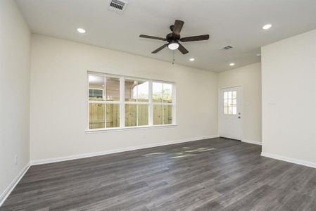 Empty room with beige walls, large windows, dark wood flooring, ceiling fan, and a door leading outside with a fenced backyard view.