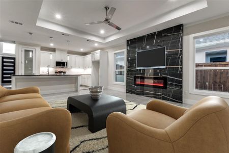 Living room featuring ceiling fan, a tile fireplace, - 24x48 fireplace porcelain tile and flooring, and a Tray ceiling