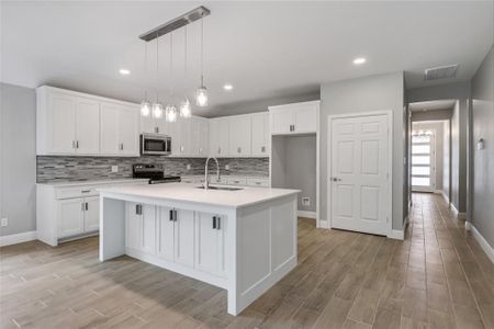 Kitchen featuring white cabinetry, appliances with stainless steel finishes, a kitchen island with sink, hanging light fixtures, and sink