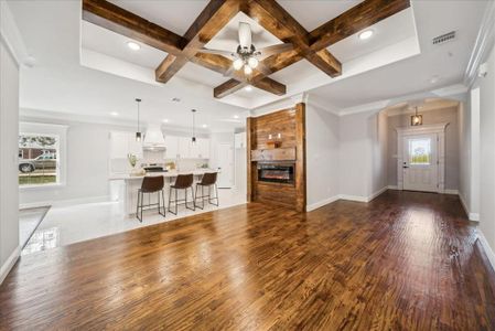 Unfurnished living room with beam ceiling, a large fireplace, ceiling fan, crown molding, and coffered ceiling