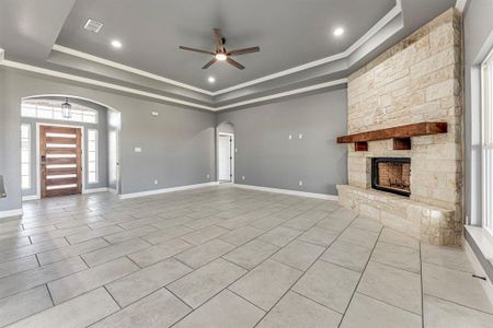 Unfurnished living room featuring a fireplace, a raised ceiling, ceiling fan, and crown molding