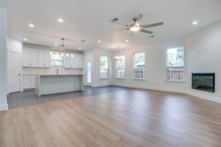 Unfurnished living room with light wood-type flooring, a wealth of natural light, sink, and ceiling fan with notable chandelier