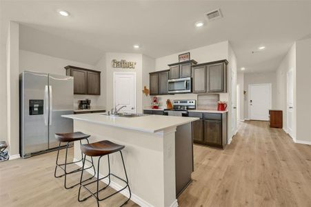 Kitchen featuring dark brown cabinetry, stainless steel appliances, sink, light wood-type flooring, and a center island with sink