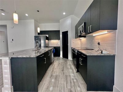 Kitchen with a large island with sink, light hardwood / wood-style floors, pendant lighting, and appliances with stainless steel finishes