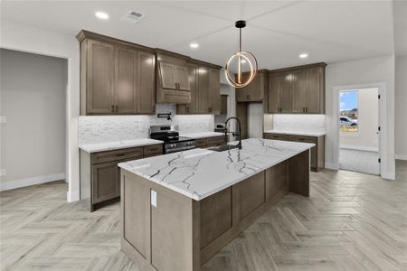 Kitchen with light stone counters, an island with sink, sink, stainless steel range, and decorative backsplash