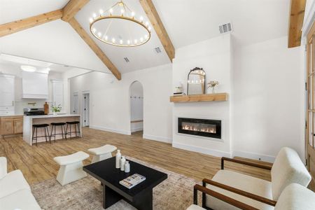 Living room with light hardwood / wood-style floors, an inviting chandelier, beam ceiling, and high vaulted ceiling