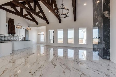 Unfurnished living room with a wealth of natural light, a notable chandelier, and high vaulted ceiling