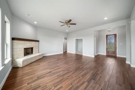 Unfurnished living room with a stone fireplace, wood-type flooring, a healthy amount of sunlight, and ceiling fan