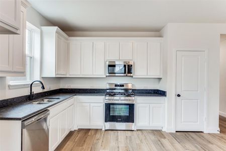 Kitchen featuring stainless steel appliances, sink, white cabinetry, and light wood-type flooring