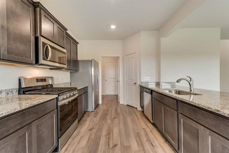 Kitchen featuring dark brown cabinets, light hardwood / wood-style flooring, stainless steel appliances, light stone counters, and sink