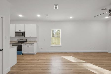 Kitchen featuring white cabinetry, ceiling fan, appliances with stainless steel finishes, light stone countertops, and light hardwood / wood-style flooring