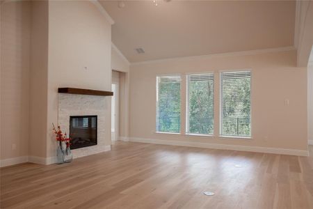 Unfurnished living room with crown molding, a stone fireplace, vaulted ceiling, and light hardwood / wood-style flooring