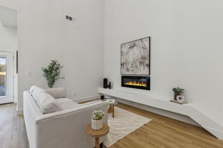 Living room with a fireplace, wood-type flooring, and a towering ceiling