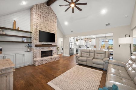 Living room featuring a fireplace, brick wall, ceiling fan with notable chandelier, and high vaulted ceiling