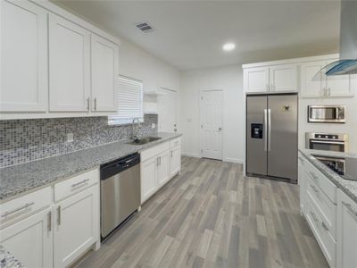 Kitchen featuring wall chimney range hood, stainless steel appliances, white cabinets, and sink