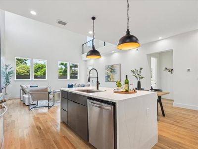 Kitchen with an island with sink, hanging light fixtures, sink, stainless steel dishwasher, and light hardwood / wood-style floors