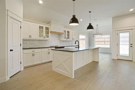 Kitchen featuring tasteful backsplash, hanging light fixtures, light hardwood / wood-style floors, a kitchen island with sink, and white cabinetry