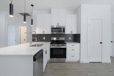 Kitchen featuring kitchen peninsula, appliances with stainless steel finishes, decorative light fixtures, white cabinets, and light hardwood / wood-style floors