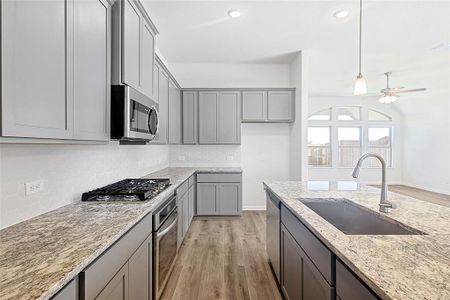 Kitchen featuring light stone countertops, appliances with stainless steel finishes, gray cabinetry, sink, and light hardwood / wood-style floors