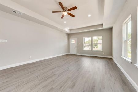 Empty room featuring ceiling fan, light hardwood / wood-style flooring, and a tray ceiling