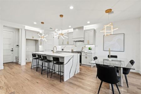 Kitchen with decorative light fixtures, custom range hood, an island with sink, light stone countertops, and stainless steel range with electric stovetop