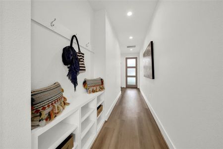 Built-in storage and coat hooks, featuring a sleek wooden floor and a frosted glass Front door.