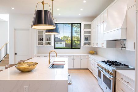 Kitchen featuring hanging light fixtures, premium range hood, white cabinetry, range with two ovens, and sink