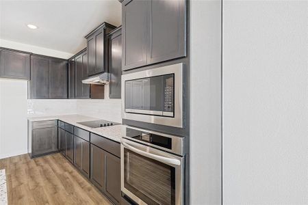 Kitchen with decorative backsplash, appliances with stainless steel finishes, light stone counters, dark brown cabinets, and light hardwood / wood-style floors