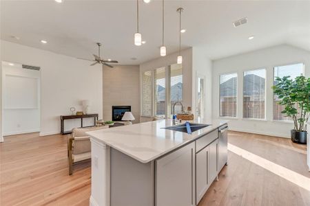 Kitchen featuring sink, a tiled fireplace, hanging light fixtures, a kitchen island with sink, and gray cabinetry