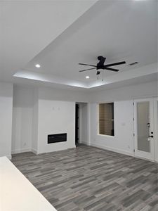 Unfurnished living room with ceiling fan, a raised ceiling, and wood-type flooring