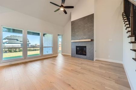 Unfurnished living room featuring ceiling fan, light hardwood / wood-style floors, a tile fireplace, and high vaulted ceiling