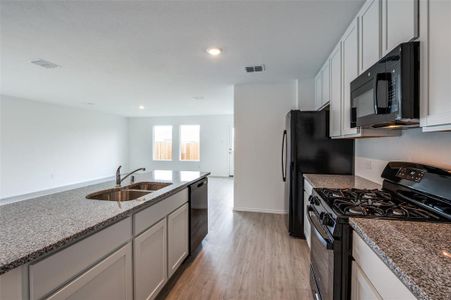 Kitchen featuring light stone counters, black appliances, sink, white cabinetry, and light hardwood / wood-style flooring