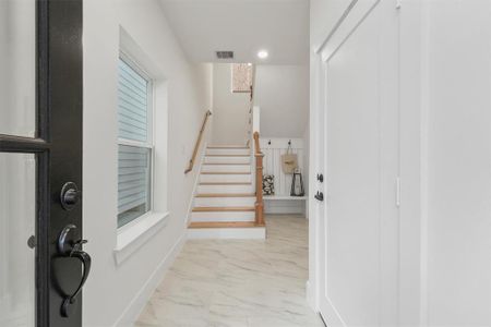 Enter thru the front door to be greeted by bright, clean entryway with a staircase leading up. The space features modern finishes with a tiled floor, natural light from a window, and a welcoming, neutral color palette.