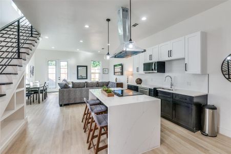 Kitchen featuring stainless steel appliances, island exhaust hood, sink, light hardwood / wood-style floors, and backsplash