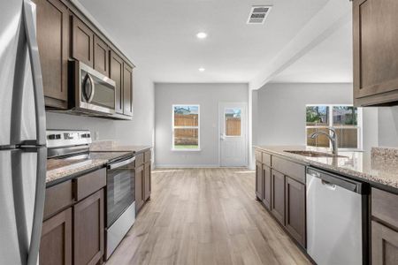 Kitchen featuring light wood-type flooring, light stone countertops, a healthy amount of sunlight, and stainless steel appliances