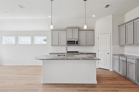 Kitchen with light wood-type flooring, tasteful backsplash, a kitchen island with sink, and stone counters