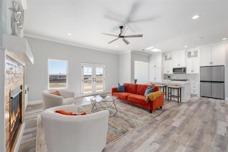 Living room with ornamental molding, ceiling fan, light hardwood / wood-style floors, and french doors