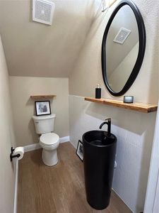 Bathroom featuring wood-type flooring, lofted ceiling, tile walls, and toilet